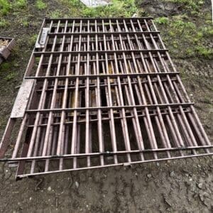 IMG_ 68091 - Montana Auctions by Kevin Hill Rusty metal grate panel lying on muddy ground outdoors, with grass and scattered debris around it.