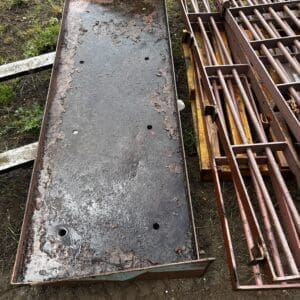 IMG_ 68093 - Montana Auctions by Kevin Hill Long rusty steel trough with peeling paint and several drainage holes sits on dirt beside rusty metal frames and cages in an outdoor yard.