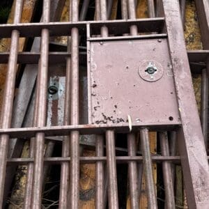 IMG_ 68094 - Montana Auctions by Kevin Hill Rusty metal grate grid with an access panel featuring a small padlock, outdoors on weathered wood.