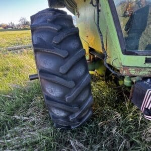 IMG_1299 - Montana Auctions by Kevin Hill Green agricultural tractor with a large ribbed rear tire parked in a grassy field, blue sky in the background and a weathered yellow panel near the cab side side view.