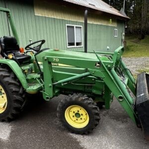 IMG_1377 - Montana Auctions by Kevin Hill Green John Deere tractor with front loader bucket parked on a paved surface near a green building; large rear tire visible.