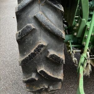 IMG_1388 - Montana Auctions by Kevin Hill Close-up of a large agricultural tractor rear tire with deep chevron tread, muddy and worn, green tractor frame visible to the right.