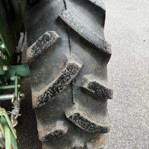 IMG_1389 - Montana Auctions by Kevin Hill Close-up of a large off-road tractor tire with deep, chunky tread on a paved surface, dirt on the lugs.