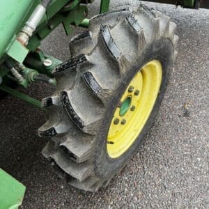 IMG_1390 - Montana Auctions by Kevin Hill Close-up of a tractor wheel with a large knobby tire and a yellow rim on green farming equipment on asphalt.