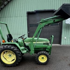 IMG_1391 - Montana Auctions by Kevin Hill Green John Deere 790 utility tractor with front-end loader bucket raised, parked on asphalt in front of a green metal building.