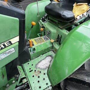 IMG_1395 - Montana Auctions by Kevin Hill Green John Deere tractor interior with a torn black seat, orange indicators, and a weathered metal foot platform full of holes and rust.