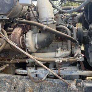 IMG_6540 - Montana Auctions by Kevin Hill Close-up of a dusty diesel engine with metal pipes, hoses, and a rusted exhaust component.