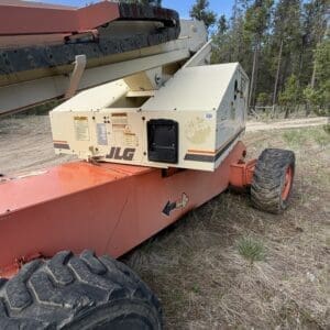 IMG_6548 - Montana Auctions by Kevin Hill JLG boom lift on a red chassis parked on dirt with trees in the background, tire visible in foreground.