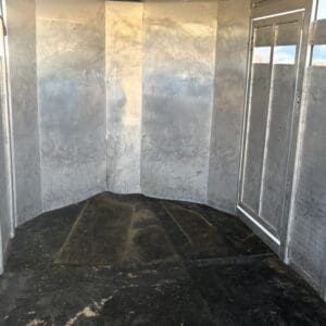 Screenshot - Montana Auctions by Kevin Hill Empty aluminum trailer interior with curved metal walls and vertical seams, and a dark scuffed floor; a metal door is visible on the right side.