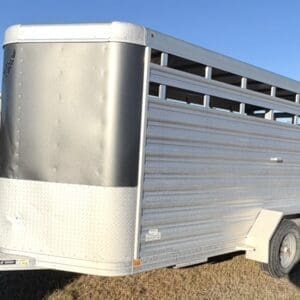 Screenshot - Montana Auctions by Kevin Hill Silver aluminum livestock trailer with two axles parked on a dry field; front hitch visible in the foreground.