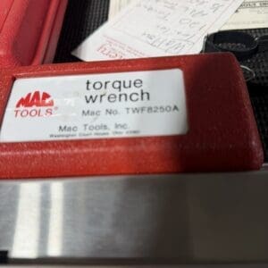 Close-up of a red tool case showing a torque wrench label with Mac Tools logo and model Mac No. TWF8250A, in a workshop scene.