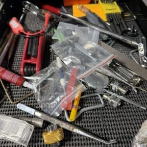 Assorted tools and small hardware scattered in a metal tool tray, including pliers, screwdrivers, wrenches, and bags of fasteners.