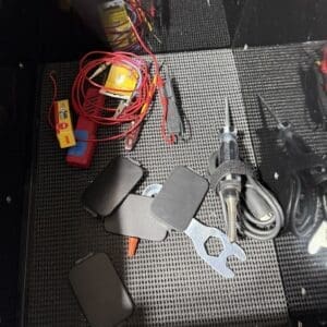 Messy toolbox drawer with red wire harnesses, a yellow module, black rectangular adapters, a blue tool case, and a wrench.