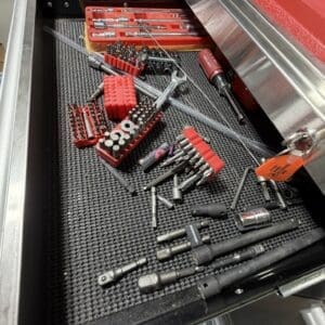 Open tool drawer displaying red bit organizers, sockets, and assorted metal hand tools on a perforated tray in a workshop.