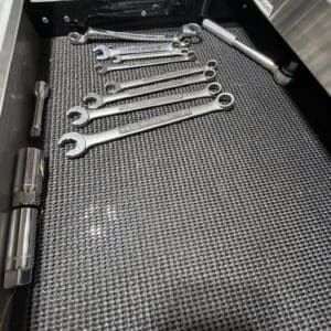 Set of combination wrenches arranged in a tray on a textured rubber mat, with a long torque wrench resting along the side.