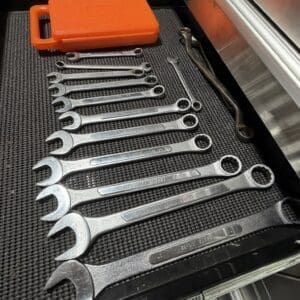 Row of large metal combination wrenches laid out in a tool tray with an orange plastic case in the background.