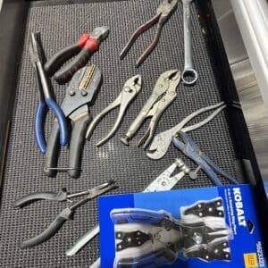 Assorted hand tools in a metal tool tray, including pliers, wrenches, and cutters, with a blue Kobalt packaging box in the corner.