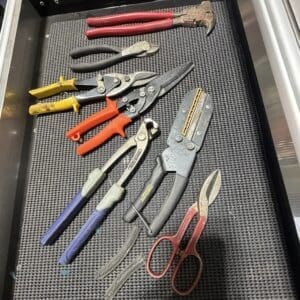 Assorted hand tools laid in a black tray: pliers, snips, cutters, and scissors with red, yellow, and blue handles.