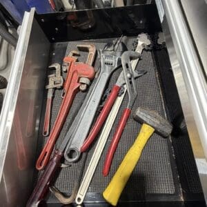 Open tool drawer with red pipe wrenches, adjustable wrenches, a yellow hammer, and screwdrivers laid out on a tray.