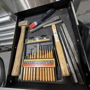 Open tool drawer containing wood-handled chisels, two hammers, files, and a small screwdriver set.