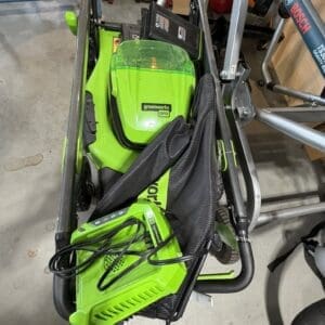 Greenworks Pro cordless leaf blower with battery and charger resting in a metal cart or frame in a workshop area.