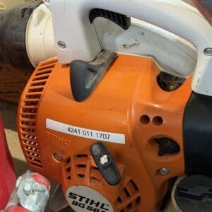 Close-up of an orange Stihl BG 56C gas blower engine with a white handle and black control switch, in a workshop setting (shows model label).