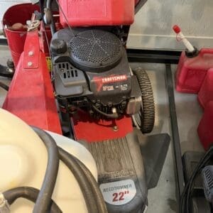 Gasoline-powered Craftsman weed trimmer with a 22-inch cutting width stored in a garage, red and black engine visible.