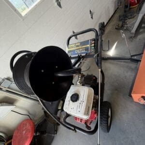 Gas-powered portable pressure washer on wheels with a spray wand, stored in a garage