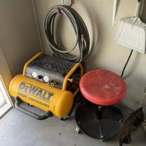 Yellow DeWalt air compressor with gauges and a coiled hose, beside a red adjustable stool in a garage workshop.