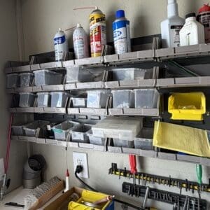 Workbench with pegboard and shelves holding small parts in labeled plastic bins, spray cans, and tools in a workshop.