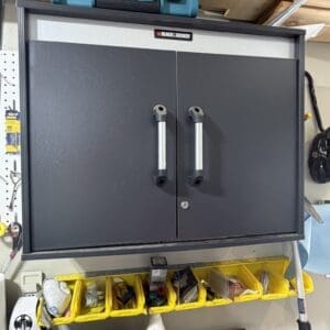 Gray wall-mounted tool cabinet with two doors and silver handles; a teal toolbox sits on top.