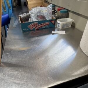 Metal workbench cluttered with a box of Skippy Creamy peanut butter cups and assorted tools near a window.