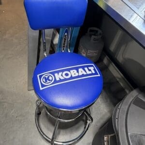 Blue Kobalt swivel stool with backrest in a workshop setting, chrome base and blue padded seat and backrest.
