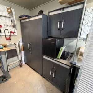 Garage workshop with tall gray storage cabinets, pegboard tools on the wall, and a small black fridge on a shelf.