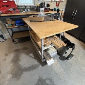 Workshop scene: a mobile workbench with plywood top and lower shelves holding wood and metal scraps