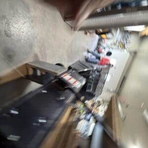 Tilted view of a cluttered workshop with a long workbench, tools, and storage boxes scattered on the floor.