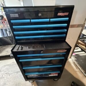 Black rolling tool chest with six blue drawers and a top work surface, labeled Channel Lock, in a workshop bay.