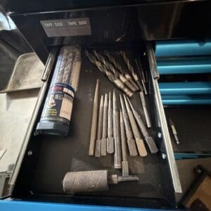 Open drawer showing drill bits, grinding tools, and a roll of tape in a metal toolbox.
