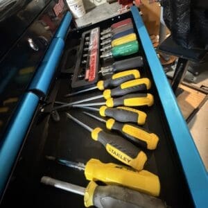 Open blue tool chest drawer showing yellow and black Stanley screwdrivers and a bit set. The organized toolkit sits in a workshop.