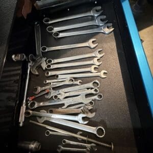 Open tool chest drawer filled with metal wrenches of various sizes and a few sockets scattered inside