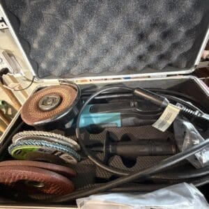 Open hard-shell case showing assorted grinding wheels and a teal angle grinder inside.