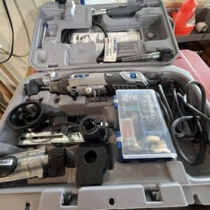 Open tool case containing a cordless drill, drill bits, and a small plastic storage box on a workbench.