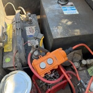 Orange portable battery jumper pack connected to a car battery with red jumper cables among tools and metal components.