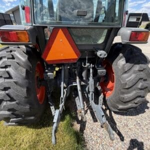 Rear view of a tractor showing three-point hitch arms, large tires, and an orange slow-moving triangle sign mounted on the back.