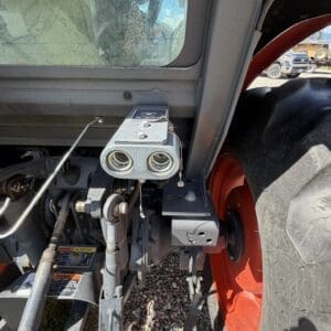 Close-up of a tractor's hitch and hydraulic quick-connects with a red wheel in the background, showing implement attachment points of the three-point hitch area.