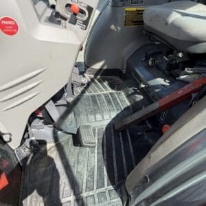 Interior of a tractor cab showing floor pedals (accelerator, brake) and a cushioned seat with controls nearby
