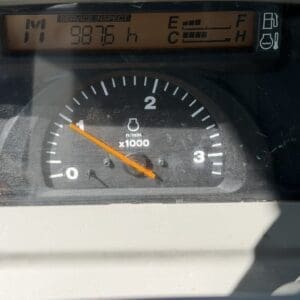 Dashboard photo showing a tachometer with the orange needle around 0.9 x1000 RPM and a digital service-inspect readout reading 9876 h, plus a low fuel indicator on the right.