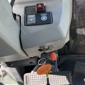 Tractor dashboard with two labeled buttons (Display Mode and Travel Speed), a red hazard switch, ignition key, and an orange key tag visible on the keychain.