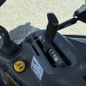 Gear shift lever with numbered settings (1–9) on a ride-on tractor, with a yellow cap and instructional diagram nearby.