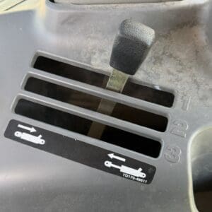 Dusty vehicle control panel close-up with a black textured lever and a label showing horizontal diagrams with arrows (numbers 1–3).